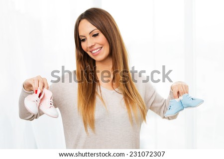 Young pregnant woman holding tiny pink and blue shoes for small child.