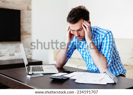 Concerned man sitting on a sofa and calculating his expenses