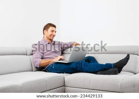 Happy young man sitting on a sofa and using a laptop