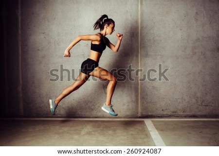 Slim attractive sportswoman running  against a concrete wall