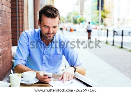 Handsome man working with smartphone and documents at outdoor cafe