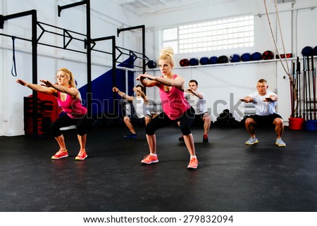 Group of young people training squats at gym class.