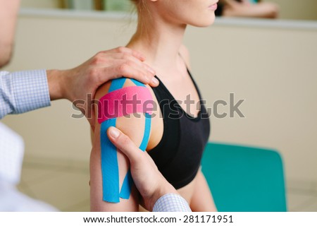 Physical therapist massages injured shoulder with kinesiotaping