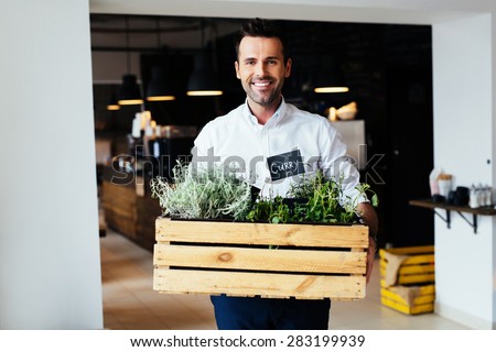Happy male restaurant manager standing with box full of fresh spices