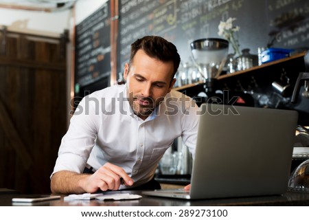 Happy cafe manager counting recipes with laptop