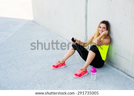 Happy woman resting after running, listening to the music on smartphone