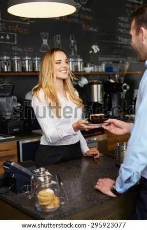 Cheerful barista giving coffee cappuccino to client in coffee shop