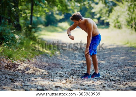 Runner resting ang checking time on watch during workout in mountains