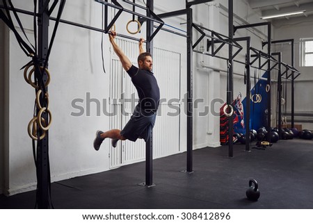 Young man doing kipping pull-ups exercise at gym