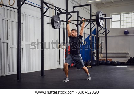 Muscular man training lunges with barbells over head