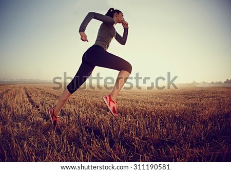 Young woman running fast on field during sunrise