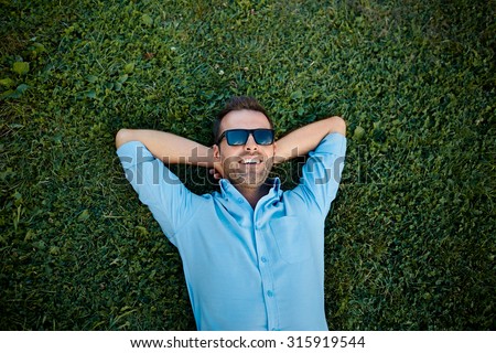 attractive man with sunglasses relaxing on the grass with his hands under the head