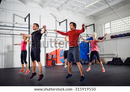 Group of people doing jumping jacks at gym