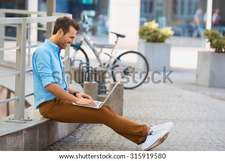 Young man sitting with laptop outside the office