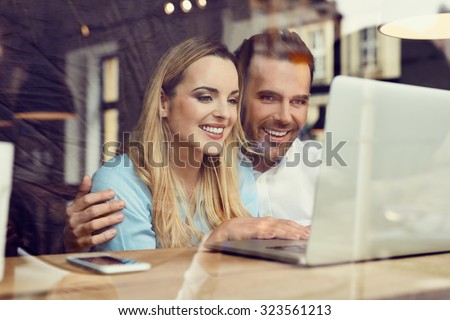 Happy couple at coffee shop looking at laptop