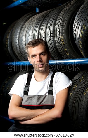 Young mechanic standing next to tire shelves in tire store