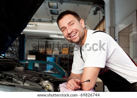 handsome mechanic based on car in auto repair shop smiling
