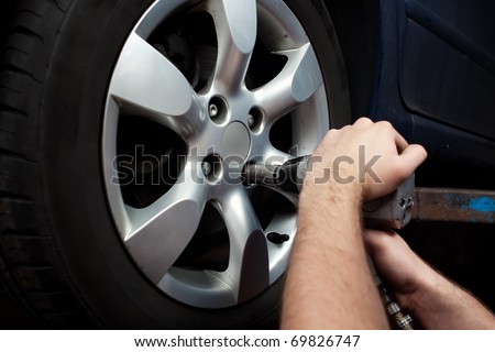 Auto mechanic changing wheel on car with pneumatic wrench.