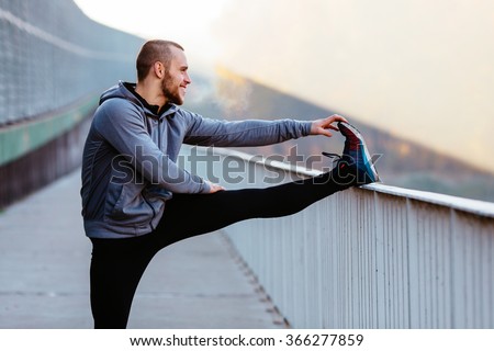 Athletic runner doing stretching exercise, preparing for morning workout in the park