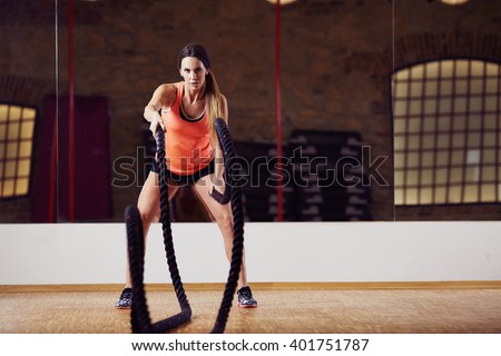Athletic woman doing battle rope exercises at gym