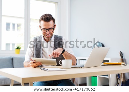 Happy man working from home using digital tablet and laptop