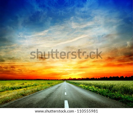 Long country road with white lines down the centre stretching off past a lone tree to the distant horizon