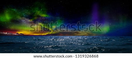 Gorgeous, unreal beautiful night view of the reflection of the northern lights in the water of the ocean and snow-capped mountains. Night Northern Lights is just an amazing sight.