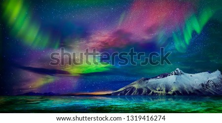 Gorgeous, unreal beautiful night view of the reflection of the northern lights in the water of the ocean and snow-capped mountains. Night Northern Lights is just an amazing sight.