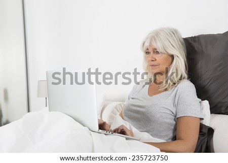 Sitting Mid Age woman with a laptop in bed
