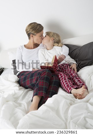 Mother and daughter kissing in bed while reading a book