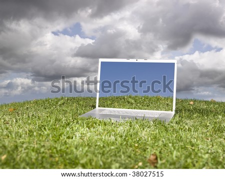 Laptop outdoors on a green field with a moody sky background