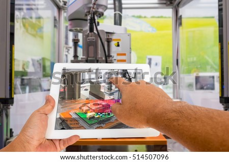 Industry 4.0 and Augmented reality for industry concept. Hand holding tablet with A/R manufacturing system control application on automate machine in smart manufacturing background.