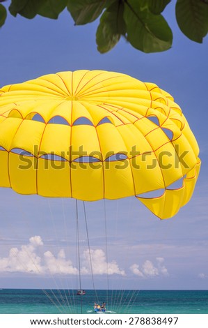 Bright yellow parachute carries it's riders from the sandy beach over the blue waters of the Andaman Sea