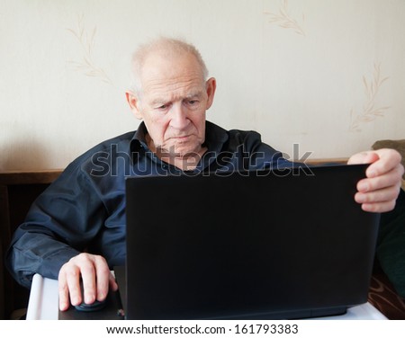 serious old man holding computer mouse - he is working on a laptop