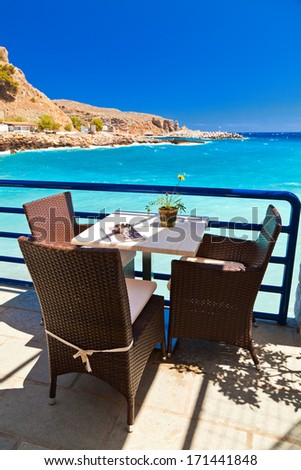 table and three chairs in a cafe in front of the blue sea