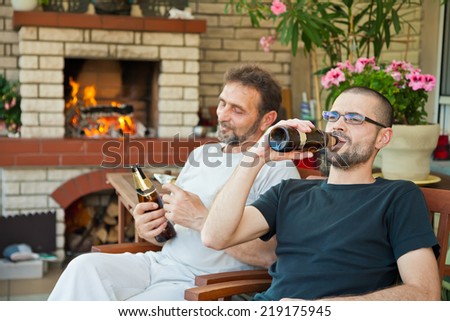 father and son sitting in front of fireplace and drinking beer