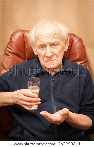 unpleased old man with a questioning look holding a glass of water and a mix of pills
