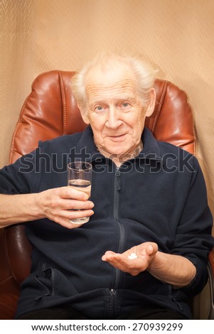 surprised old man with a questioning look holding a glass of water and a mix of pills