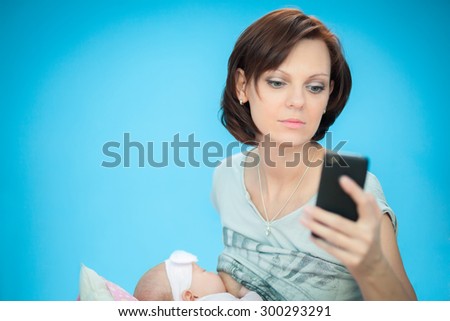adult woman breastfeeding her newborn daughter while searching something in her smartphone