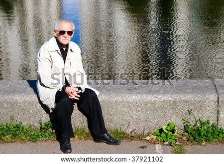 portrait of the old sad man sitting alone near the river