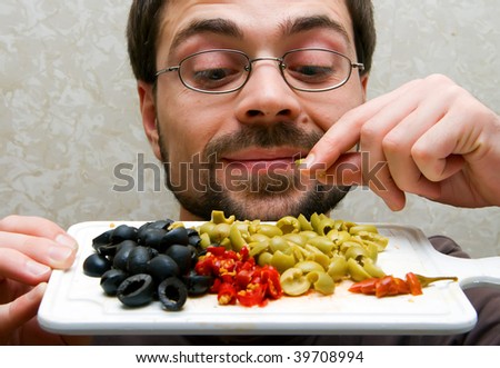 closeup male holding plate with cut green and black olives and hot pepper