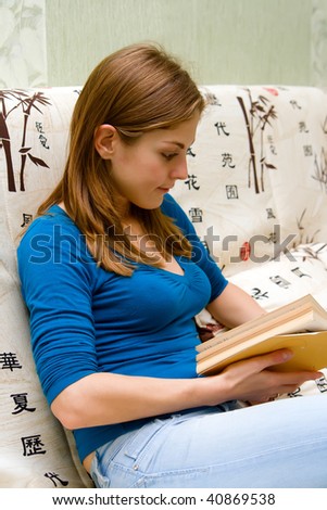 portrait of a young beautiful woman, sitting on a sofa and reading the book