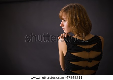 a black dressed woman with black background in the studio, is turning her back