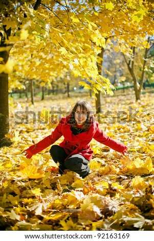 Young laughing woman in red coat playing with the falling leaves