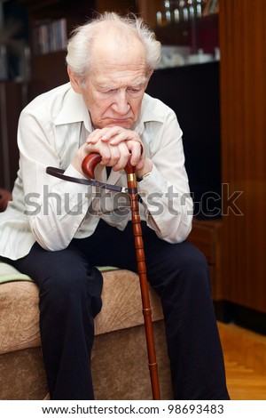 unhappy old man sitting on a bed and holding his cane