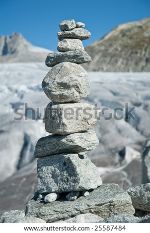 High stacked rock with blue sky and blurred glacier as background.