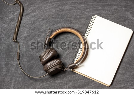 Blank notepad and headphones on black scratched chalkboard background. Top view. mockup, flat lay