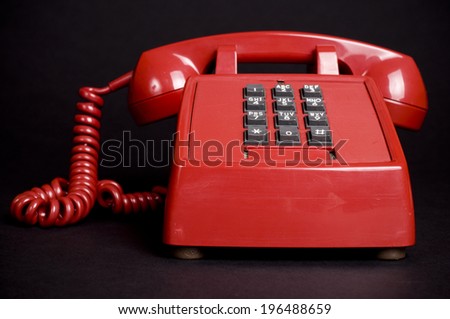 A red corded phone with push button numbers.