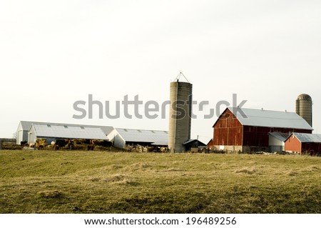 A farm land with five farm houses and two silos in the background.