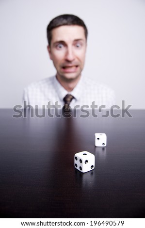A man with a surprised look views a pair of dice on a table.